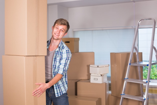 Mudança para um novo apartamento. Jovem alegre segurando uma caixa de papelão e sorrindo para a câmera enquanto