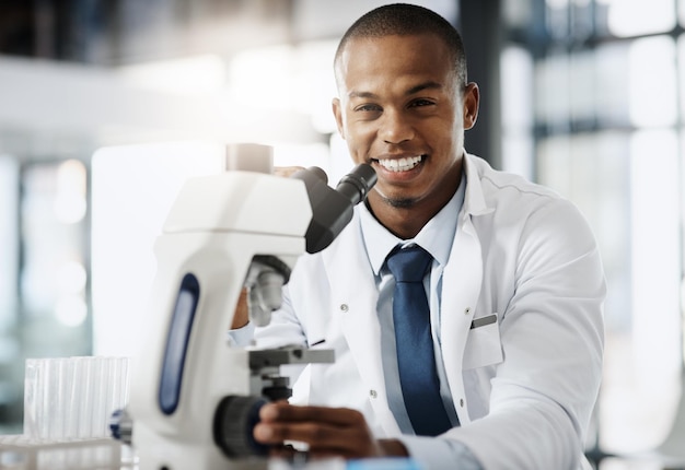 Mudando o mundo uma descoberta de cada vez Retrato recortado de um belo jovem cientista usando um microscópio enquanto fazia pesquisas em seu laboratório