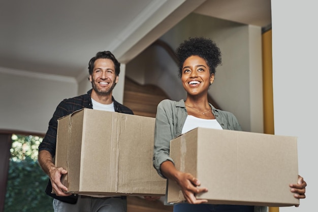 Mudanza de casa nueva y pareja feliz cargando cajas mientras se siente orgullosa y emocionada de comprar una casa con un préstamo hipotecario Esposo y esposa interraciales compradores por primera vez desempacando en la casa de sus sueños