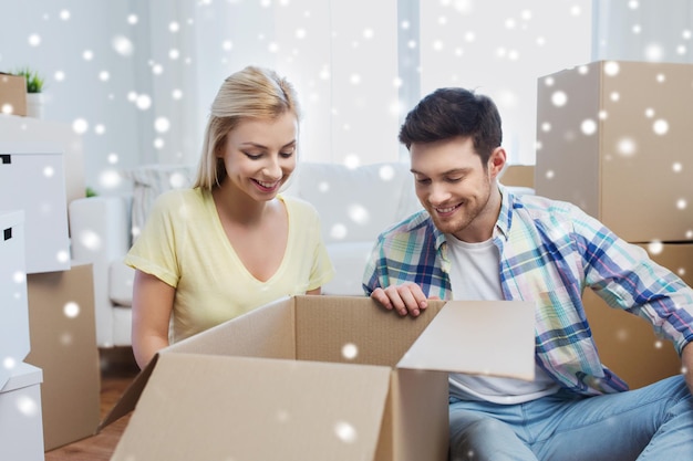 mudanza, gente, reparación y concepto inmobiliario - pareja sonriente mirando una gran caja de cartón en un nuevo hogar sobre la nieve