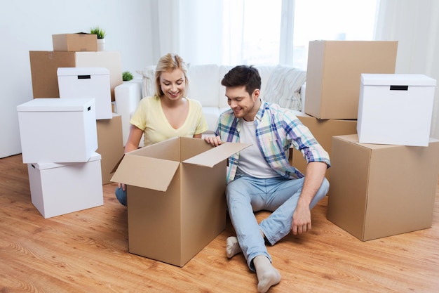 mudanza, gente, reparación y concepto inmobiliario - pareja sonriente mirando una gran caja de cartón en un nuevo hogar