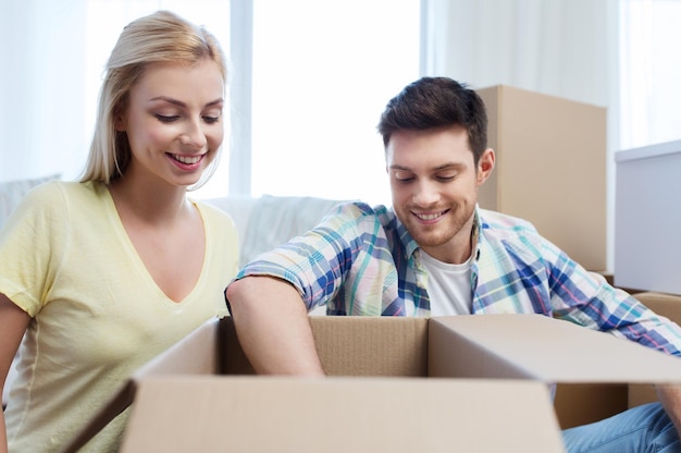 mudanza, gente, reparación y concepto inmobiliario - pareja sonriente mirando una gran caja de cartón en un nuevo hogar