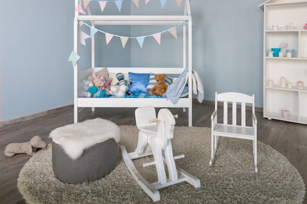 Foto muebles elegantes en una espaciosa habitación infantil monocromática. interior de dormitorio moderno con una pequeña cama de bebé decorada. caballo mecedora tradicional