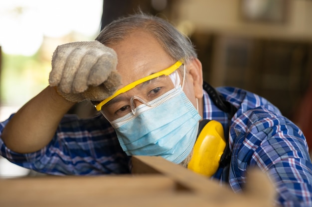 Müde erschöpfte ältere asiatische Arbeit harte Arbeit an heißen Orten, die den Kopfschweiß abwischen, Gesichtsmaske für COVID-19 und Staubschutz.