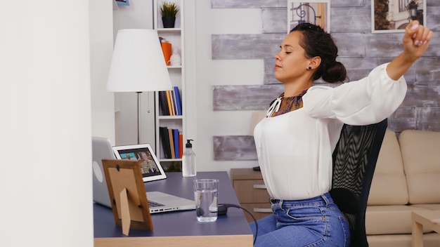 Müde Frau im Home Office, die ihren Rücken ausdehnt.