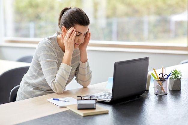 müde Frau mit Laptop, die im Heimbüro arbeitet
