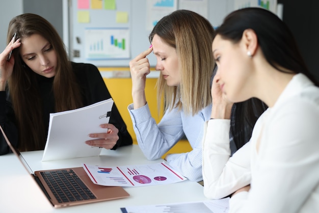 Müde Frauen sitzen am Tisch mit Dokumenten in der Hand