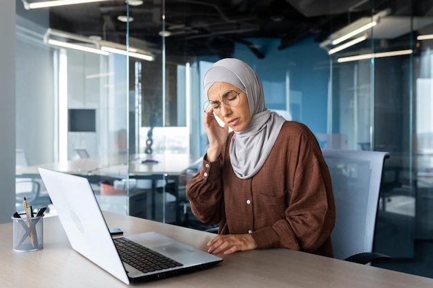 Müde Geschäftsfrau, die am Arbeitsplatz im Büro arbeitet, muslimische Frau mit Hijab ist schwer krank