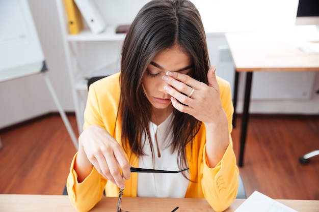 Müde Geschäftsfrau, die an ihrem Arbeitsplatz im Büro sitzt