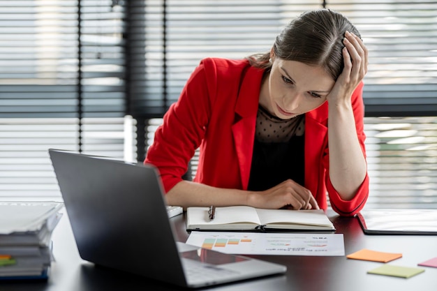 Müde Geschäftsfrau mit den Händen auf dem Kopf sitzt am Schreibtisch im Büro