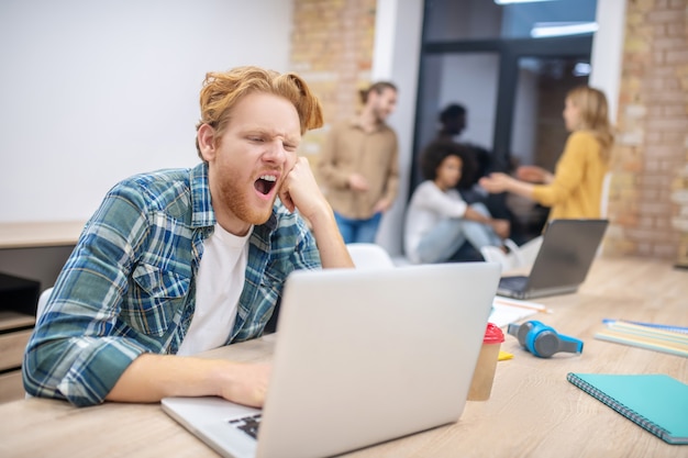 Müde. Ingwer Kerl, der an einem Laptop arbeitet und gähnt