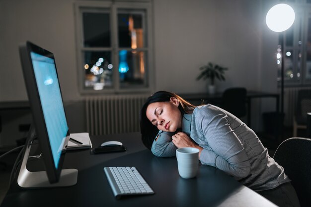 Müde junge Frau schlafen beim Arbeiten über die Zeit hinaus ein.