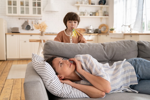 Müde junge Mutter, die mit kleinem Kind wach ist, macht Geräusche erschöpfte Mutter, die auf dem Sofa liegt, versucht zu schlafen oder sich auszuruhen