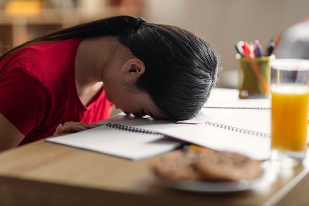 Müde, schläfrige junge chinesische Studentin liegt und schläft auf dem Tisch mit Notizbüchern im Innenraum aus nächster Nähe