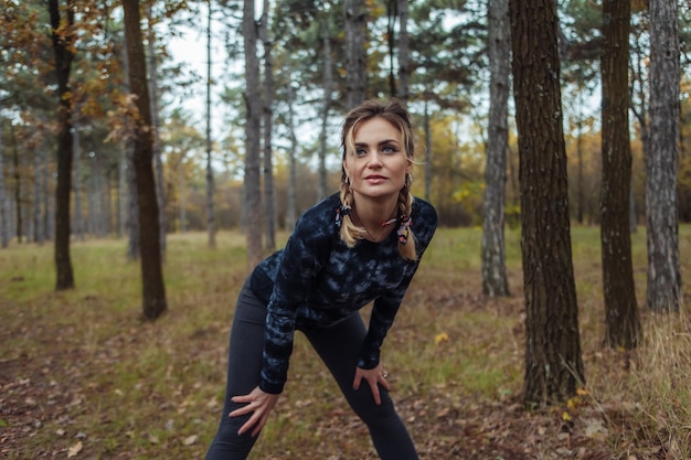 Müde Sport fit Frau mit Zöpfen, die nach dem Joggen im Herbstwald ruhen