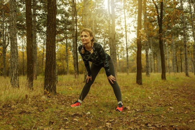 Müde Sport-Fit-Frau mit Zöpfen, die sich nach dem Joggen im Herbstwald ausruhen. Gesundes Lebensstilkonzept