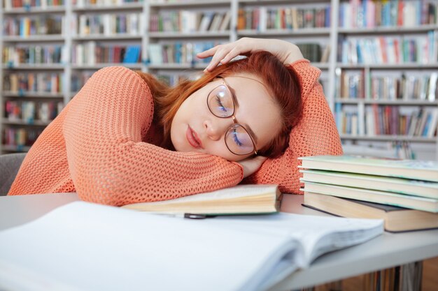 Müde Studentin, die nach dem Studium in der Bibliothek auf ihrem Schreibtisch schläft