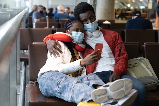 Müde Touristenpaare in Maske am Flughafen warten auf Flugverspätung aufgrund von Covid-Sperrung