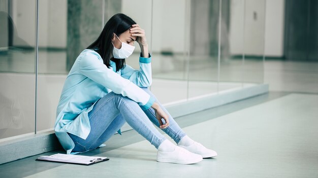 Müde und unglückliche junge Ärztin in Sicherheitsmaske in Stress nach fehlgeschlagener Arbeit