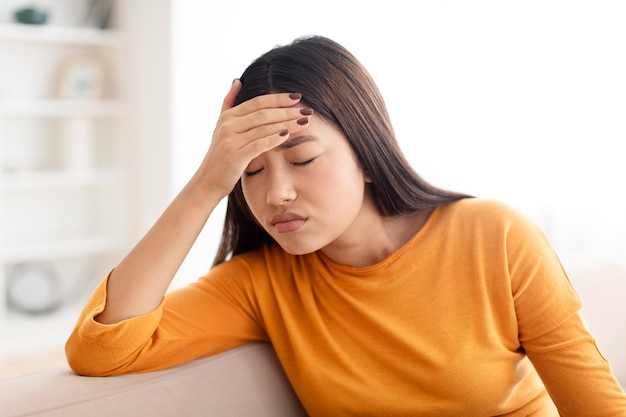 Müde unglückliche junge schöne asiatische Frau hat zu Hause Kopfschmerzen