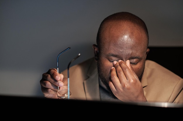 Müder afrikanischer Geschäftsmann, der sich während der Nachtarbeit die Augen reibt