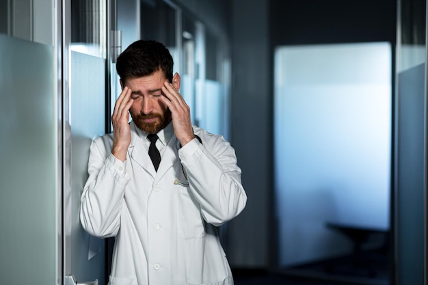 Müder Arzt, überarbeitet bei der Arbeit, hat starke Kopfschmerzen, fühlt sich schlecht, ein Mann im Korridor der Klinik ist vom Ergebnis enttäuscht