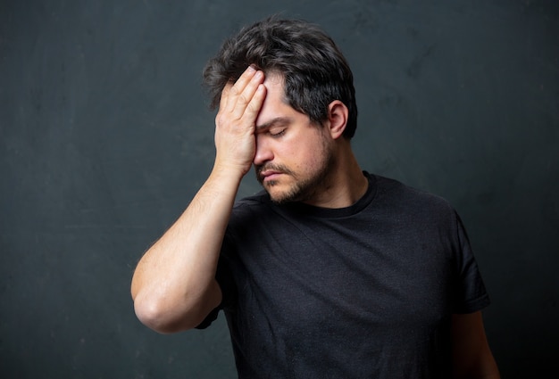 Müder Brunet-Mann im schwarzen T-Shirt auf dunkler Wand