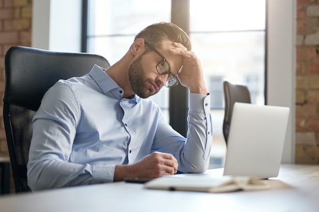 Müder Büroangestellter, der auf den Laptopbildschirm schaut