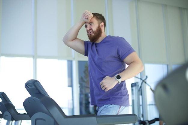 Müder, erschöpfter junger Mann fühlt sich beim Laufen auf dem Laufband im Fitnessstudio schlecht und ungesund