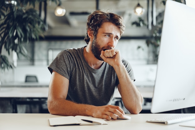 Müder Geschäftsmann, der an seinem Computer im offenen Raumbüro arbeitet. Ende des Arbeitstages