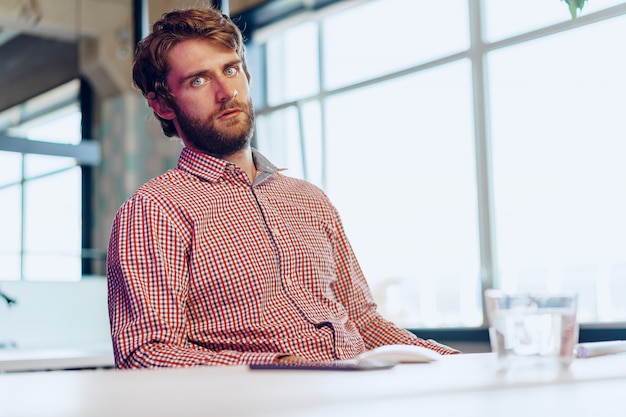 Müder Geschäftsmann, der an seinem Computer im offenen Raumbüro arbeitet. Ende des Arbeitstages