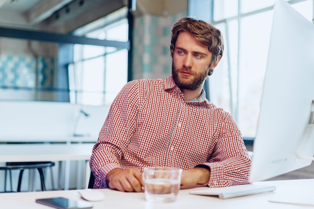 Foto müder geschäftsmann, der an seinem computer im offenen raumbüro arbeitet