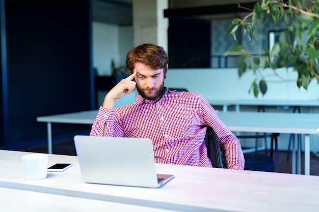 Müder Geschäftsmann, der an seinem Computer im offenen Raumbüro arbeitet