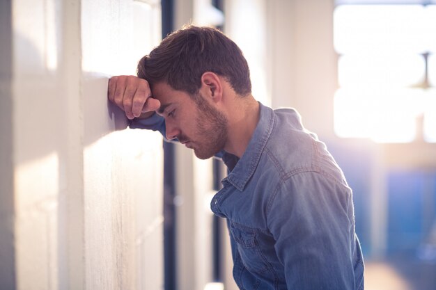 Müder Geschäftsmann, der an Wand lehnt