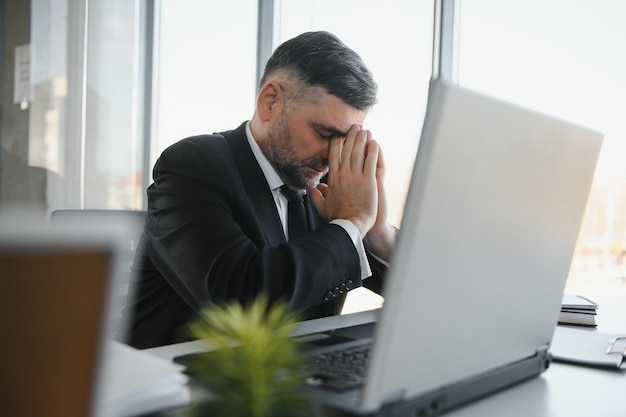 Müder gestresster Büroangestellter, der am Schreibtisch sitzt und denkt, er reibt sich die Augen und fühlt sich erschöpft