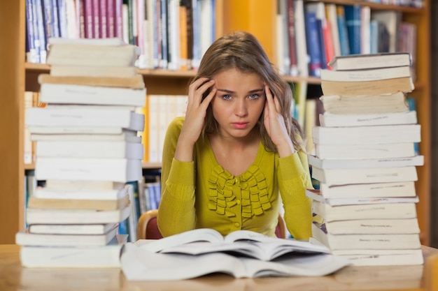 Müder hübscher Student, der zwischen Stapel von Büchern studiert