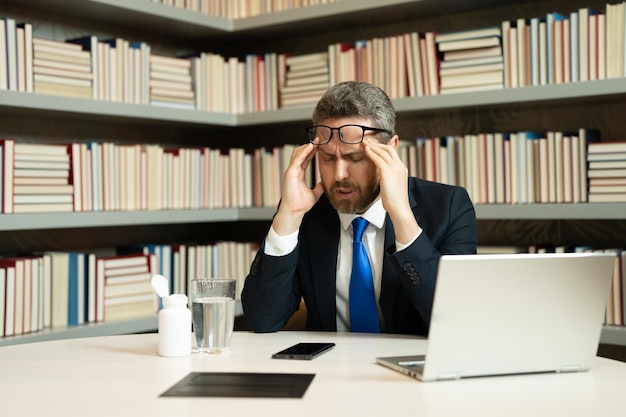 Müder Mann, der nach Computerarbeit unter Kopfschmerzen leidet, erschöpft mit geschlossenen Augen, die den Kopf berühren