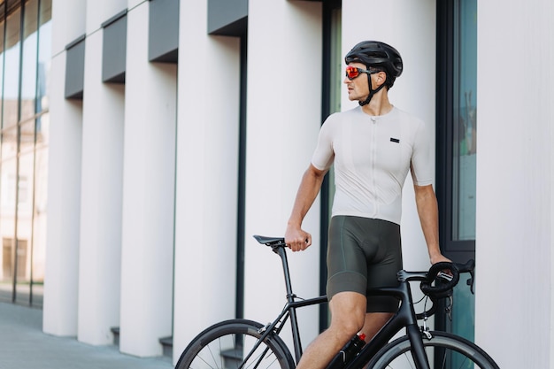 Müder Mann in Sportkleidung, Schutzhelm und verspiegelter Brille, der sich nach intensivem Training auf den Straßen der Großstadt auf dem Fahrrad entspannt Konzept des Menschensports und der Erholung
