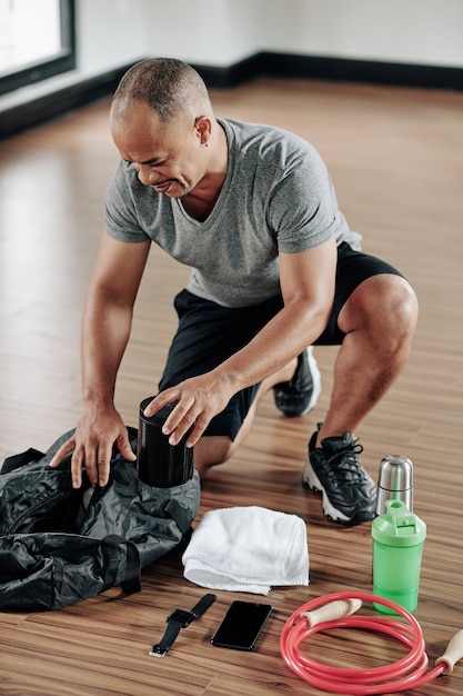 Müder Mann runzelt die Stirn vor Muskelschmerzen beim Packen der Sporttasche nach dem Training