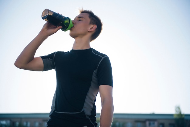 Müder Sportler Mann, der Wasser von einem Schüttler trinkt