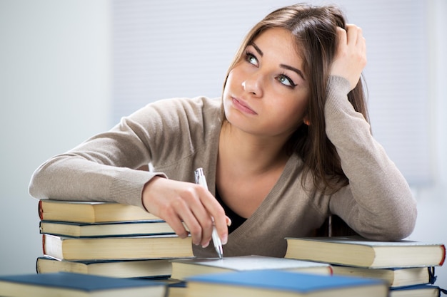 Müder Student, der mit vielen Büchern sitzt, mit ihrem Kopf in der Hand.