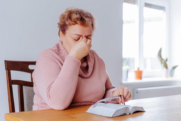 Foto müdige und traurige ältere frau zu hause kämpft mit müdigkeit, während sie ein buch liest, an dem eine alte frau sitzt