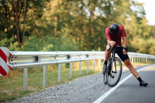 Foto müdiger radfahrer mit helm und sportkleidung ruht auf dem fahrrad in der grünen natur