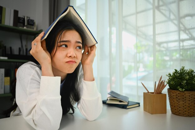 Müdiges College-Studentin legt ein Buch auf den Kopf und schaut beiseite Menschen Bildung und