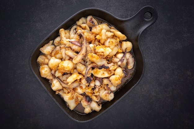 Muek Tod Kra-Tiam Prik-Thai, comida tailandesa, calamares fritos con ajo y pimienta en una sartén negra sobre fondo de textura de tono oscuro, vista superior