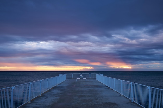 Muelle desierto con un cielo dramático sobre un mar tormentoso y oscuro al amanecer.