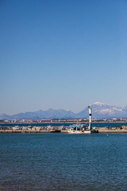 Muelle con un hermoso faro blanco y un muelle con muchos barcos y yates en el fondo del mar azul