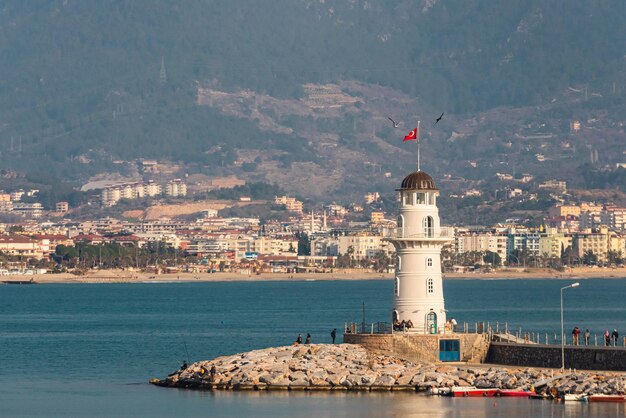 Un muelle con un hermoso faro blanco y un muelle con muchos barcos y yates en el fondo del mar azul