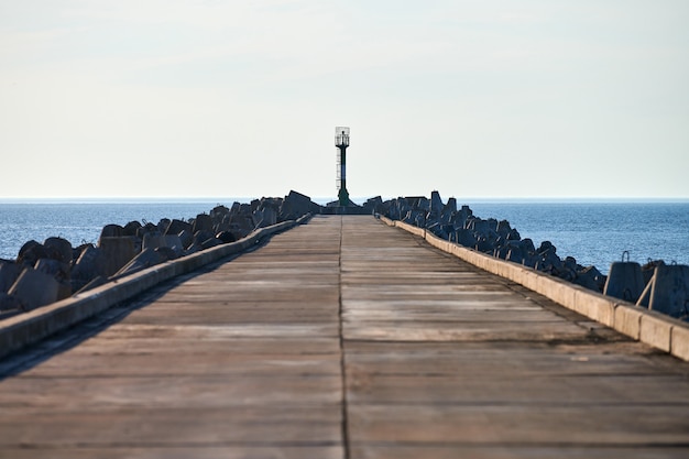 Muelle de hormigón armado largo vacío con faro de señales en el puerto en algún lugar de Europa, copie el espacio. Rompeolas de cerca, cielo azul claro, paisaje marino, horizonte, fondo hermoso mar azul tranquilo