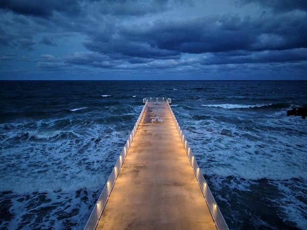 Muelle iluminado con un cielo dramático sobre un mar tormentoso y oscuro al atardecer